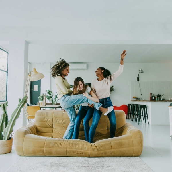 Diverse group of female friends enjoying party and laughing together - Women friends having fun at home dancing on the couch - Happy lifestyle and friendship concept